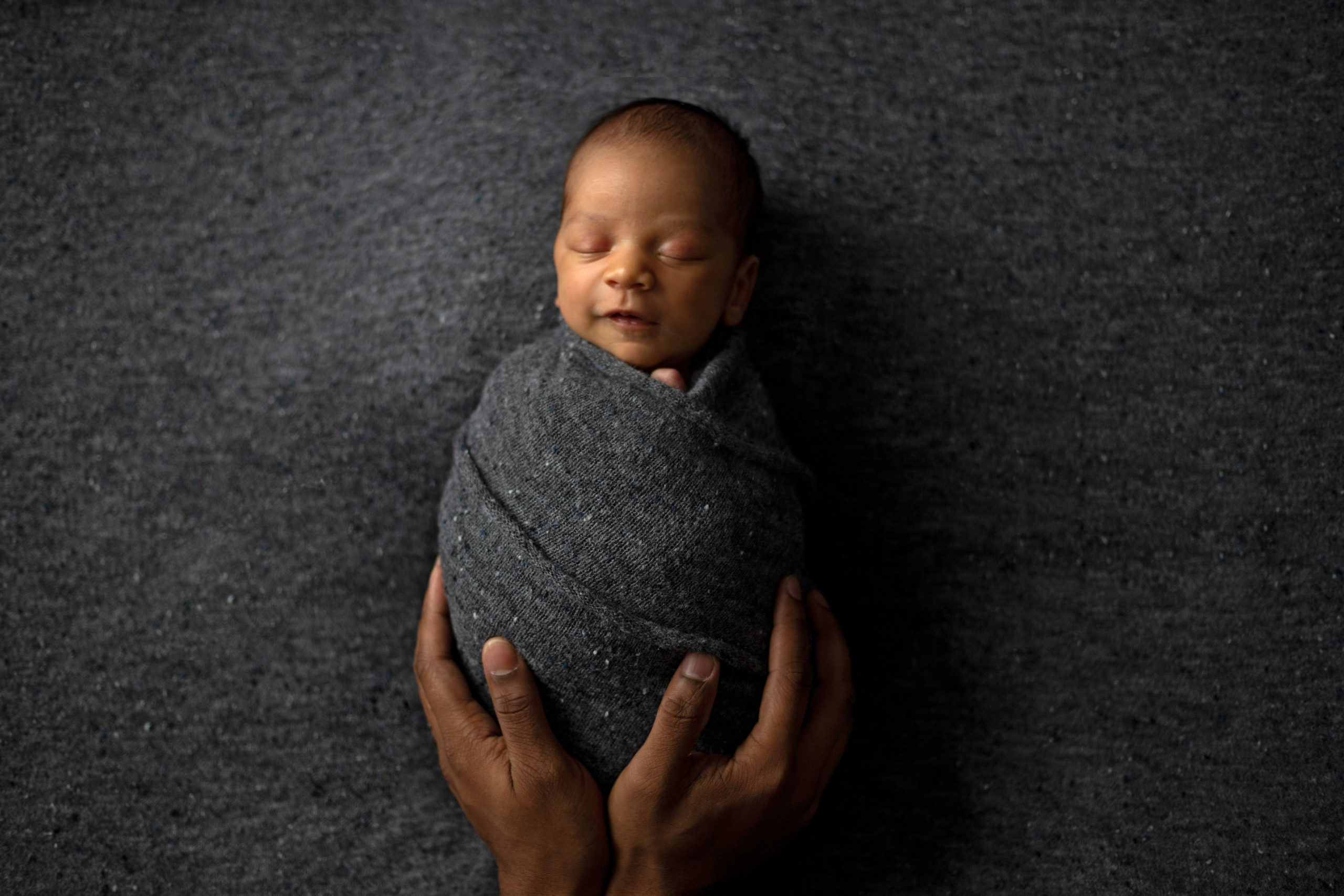 This image shows a swaddled baby being held by his dad's hands.